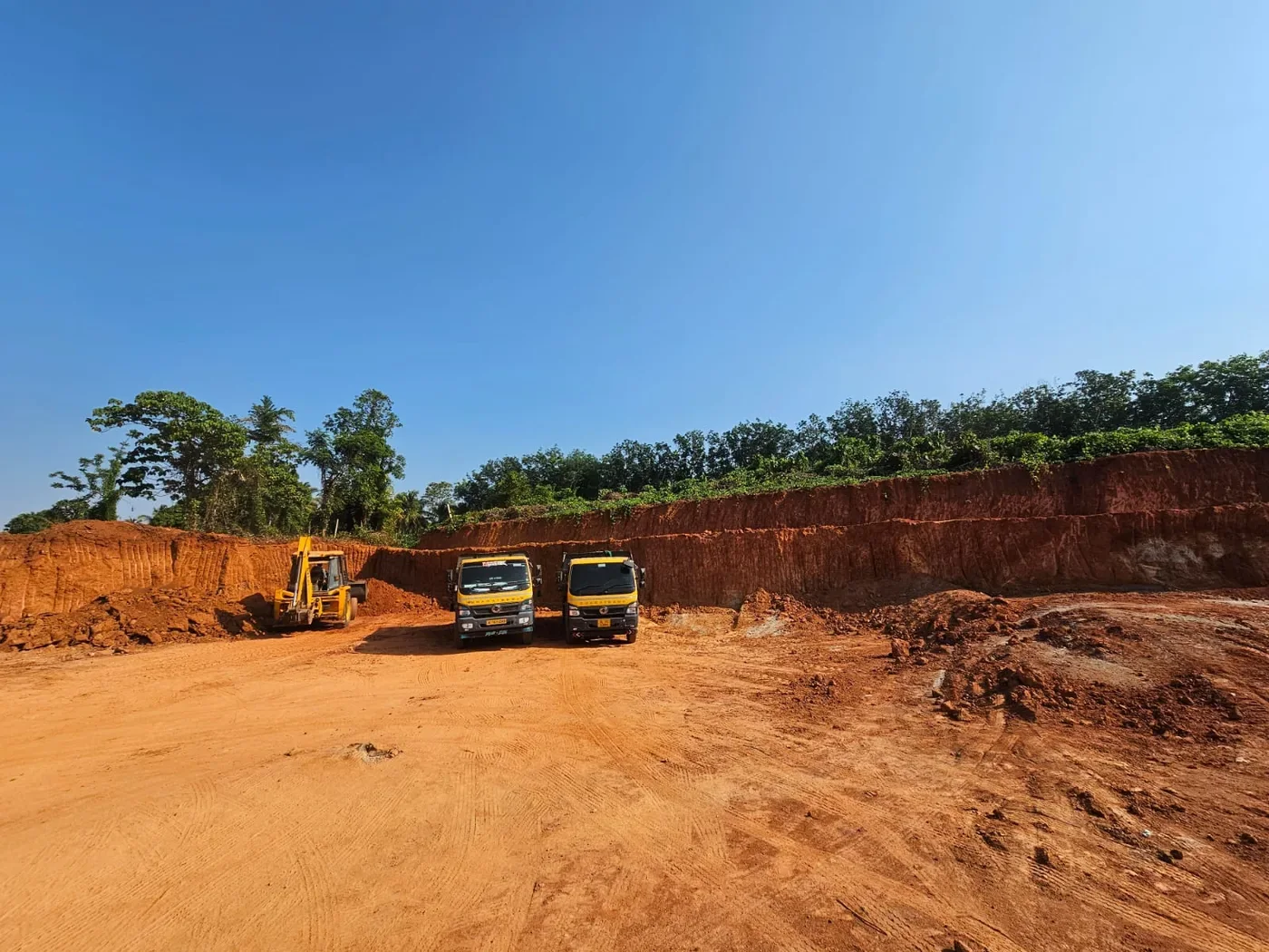 Tipper trucks and a backhoe loader at an excavated earth site.